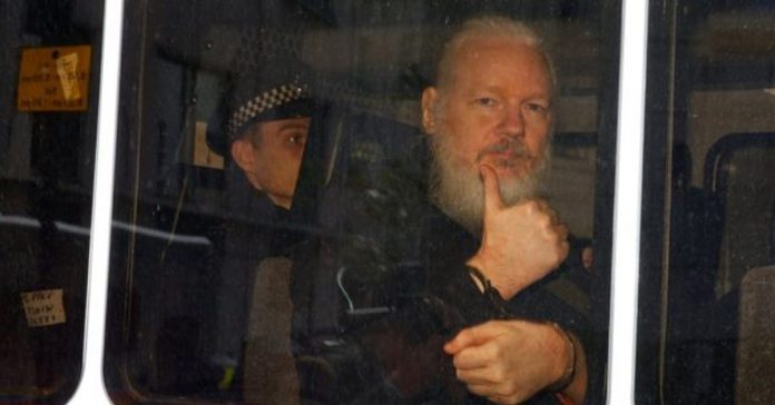លោក Julian Assange លើក​មេដៃ​នៅ​ក្នុង​ឡាន​ប៉ូលិស។ Credit: REUTERS